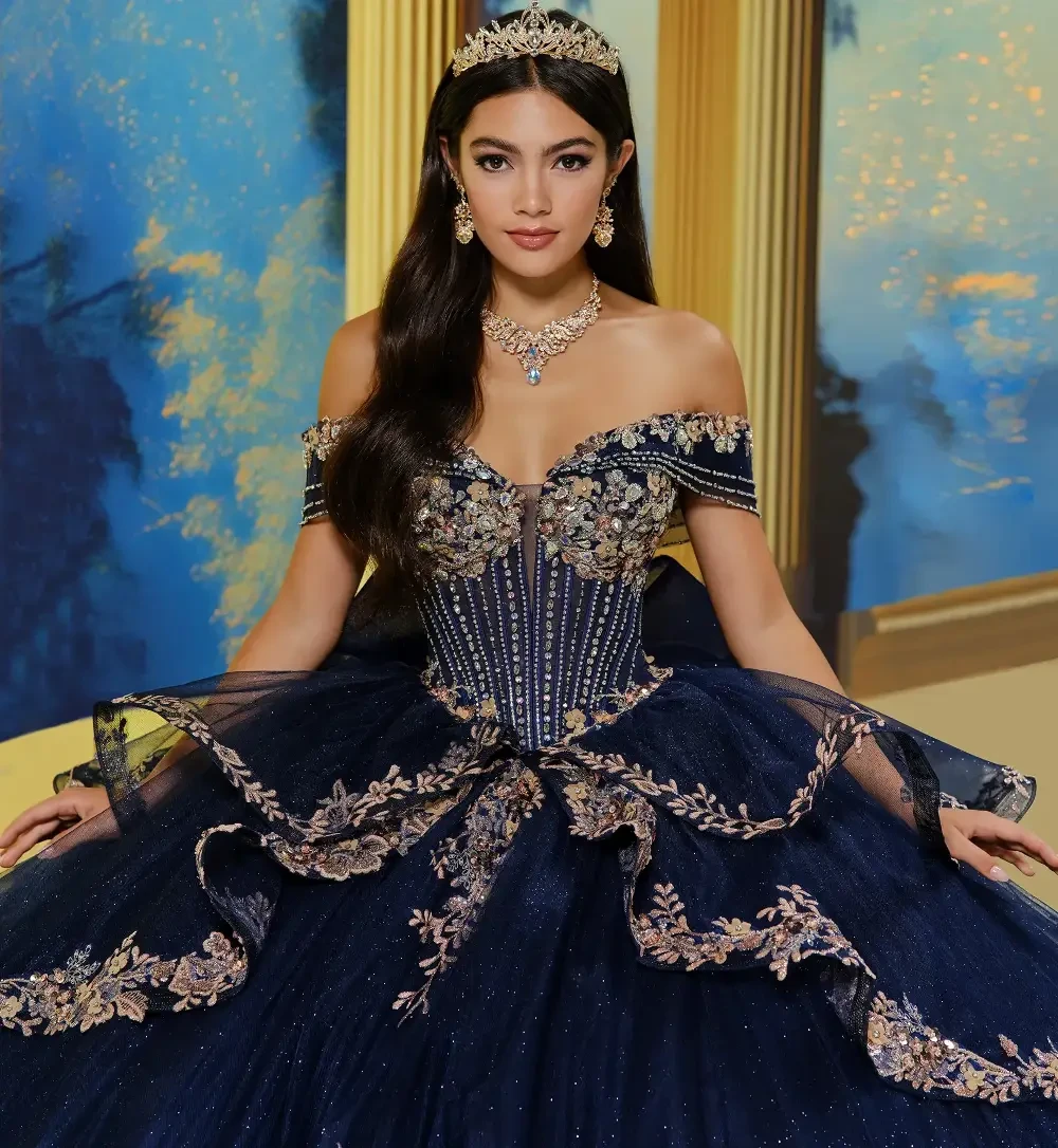 A young woman in an elegant, off-shoulder navy blue gown adorned with floral embroidery, wearing a tiara and jewelry.