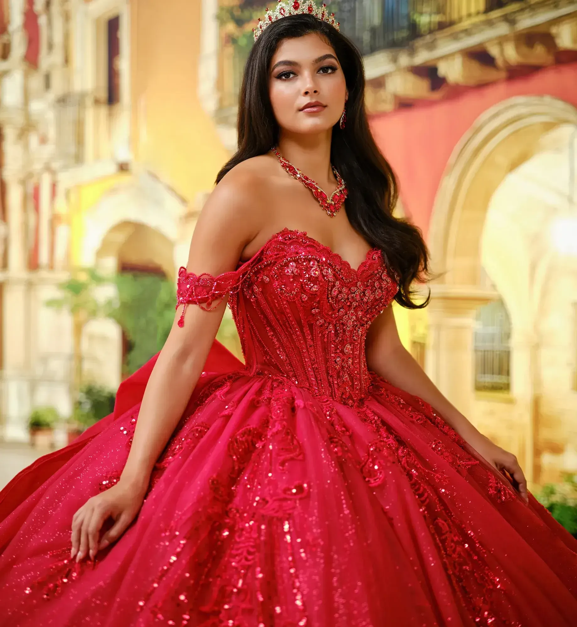A woman wearing an extravagant red gown with intricate beading and a tiara, standing in a grand setting.